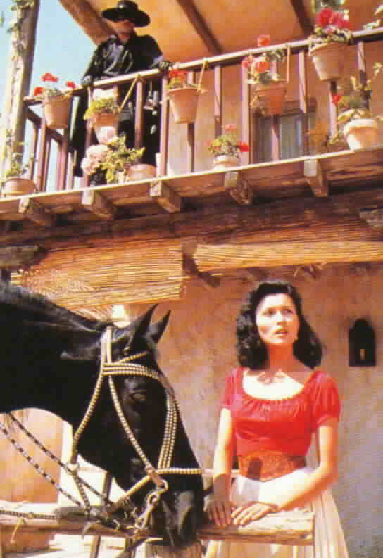 Victoria in front of the tavern with Zorro above on the second floor balcony